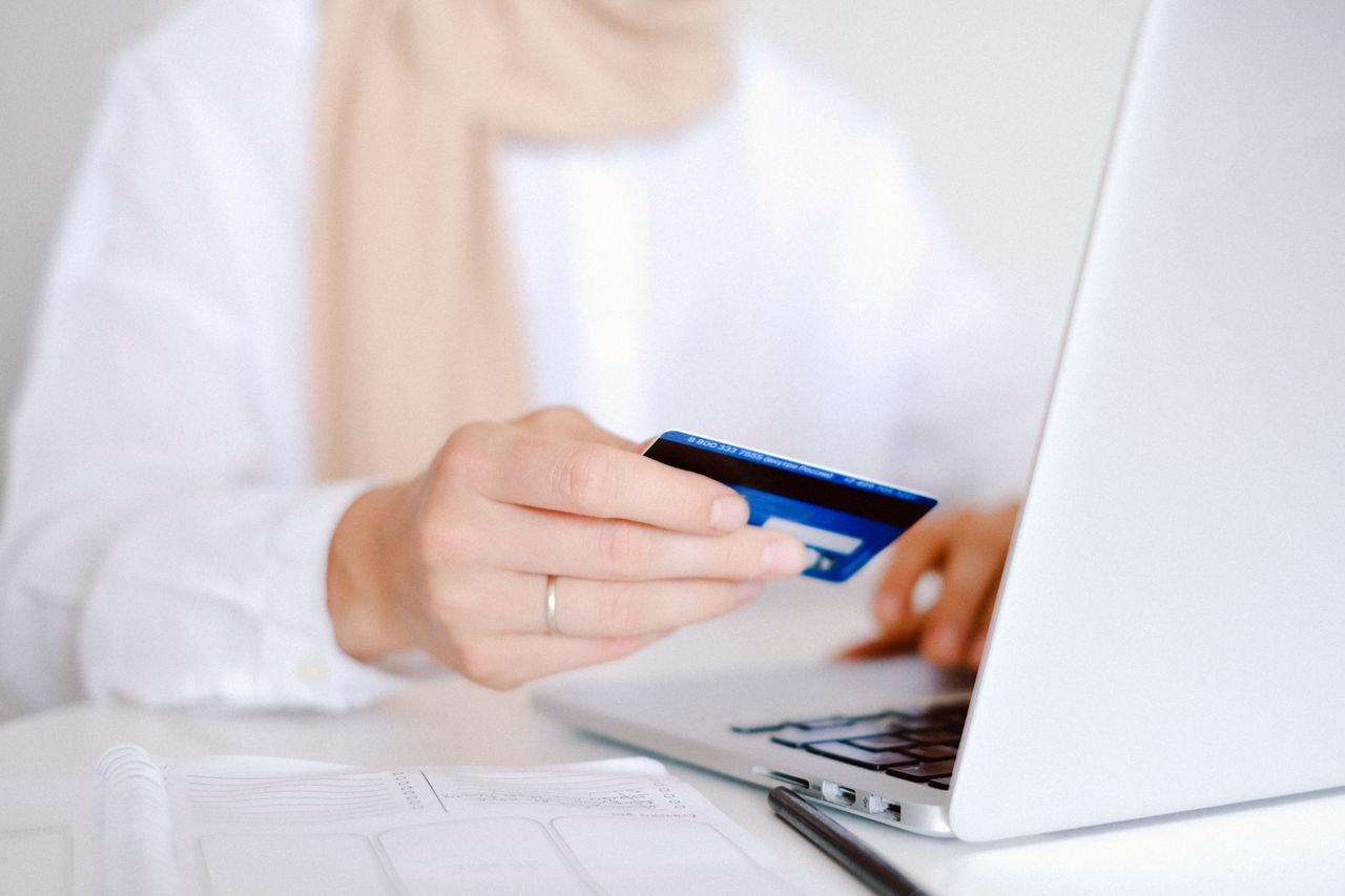 Person holding a blue credit card while paying on a laptop