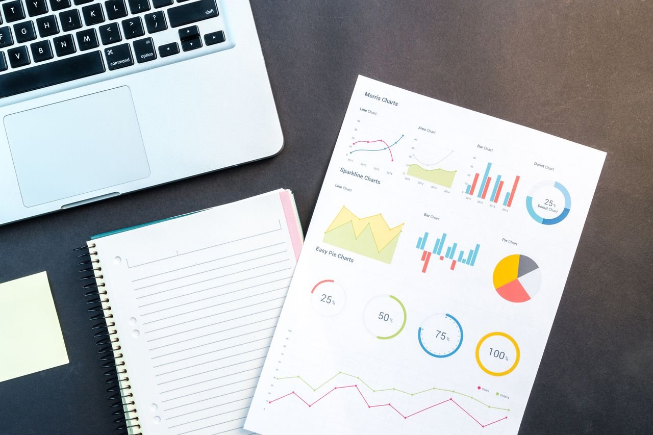 Laptop beside a printed analytics report with colorful charts and a notebook