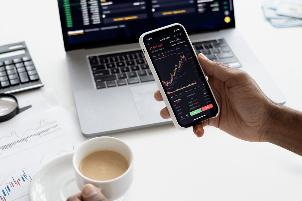 Hand holding a phone showing a live data chart beside a laptop