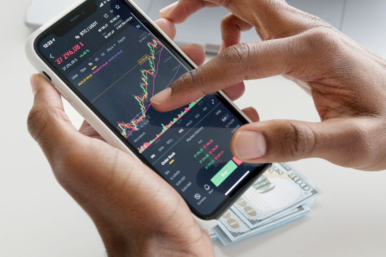 Hands tapping a live data chart on a smartphone over cash